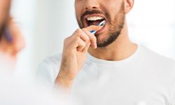Closeup of man in white shirt flossing his teeth