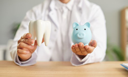 Dentist holding large model tooth and blue piggy bank