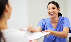 Woman in blue scrubs handing pen and clipboard to patient