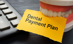 Artificial teeth biting yellow paper reading “Dental Payment Plan”