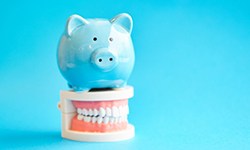 blue piggy bank sitting on top of a set of false teeth 