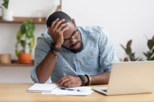 Stressed man sits in front of a laptop with head in hand