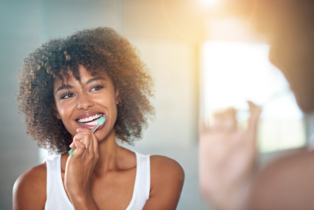 Woman in white shirt smiling while brushing her teeth